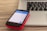 A smartphone with a visible Skype app screen is placed on a red case, resting on top of a closed laptop on a wooden surface. The laptop has a black keyboard and a silver body.