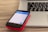 A smartphone with a visible Skype app screen is placed on a red case, resting on top of a closed laptop on a wooden surface. The laptop has a black keyboard and a silver body.