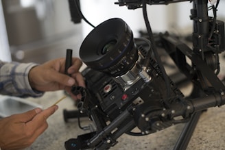 A large camera setup is being adjusted by a person using a small tool. The camera is mounted on a sophisticated rig with multiple components for stabilization and control.
