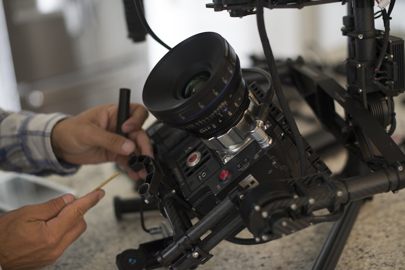 A large camera setup is being adjusted by a person using a small tool. The camera is mounted on a sophisticated rig with multiple components for stabilization and control.