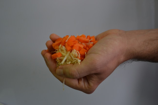 A smiling hand placing freshly cut vegetables into a clean, eco-friendly packaging box.