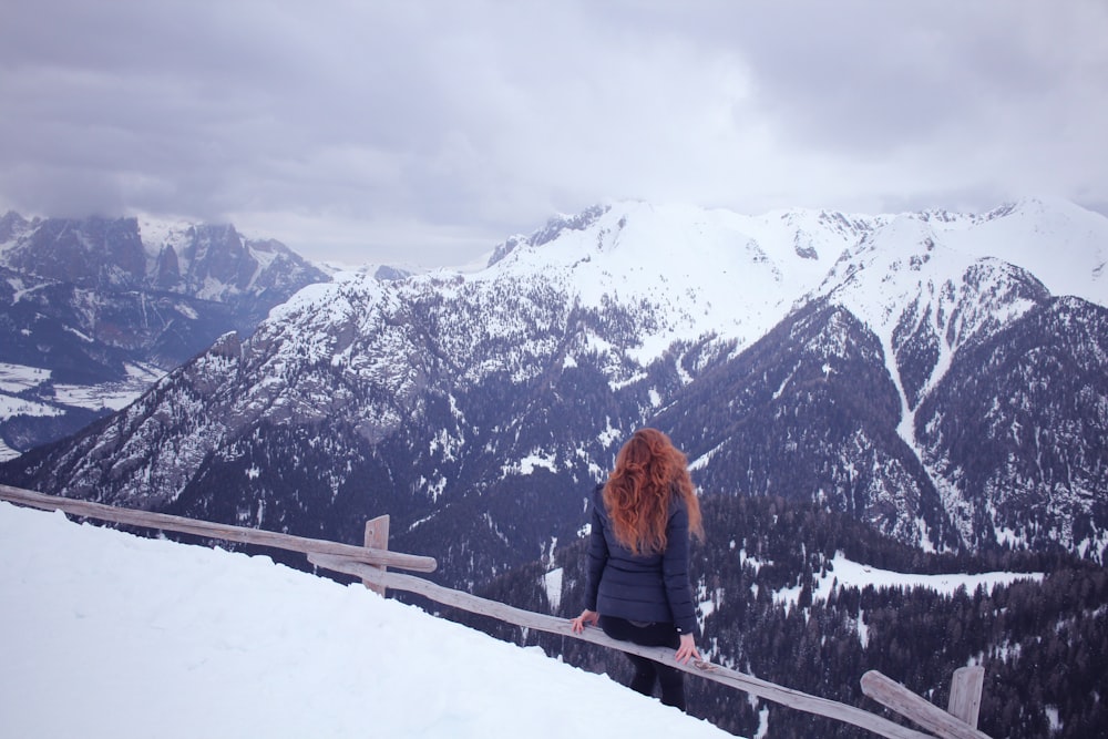 Frau sitzt auf grauem Zaun, umgeben von Schnee
