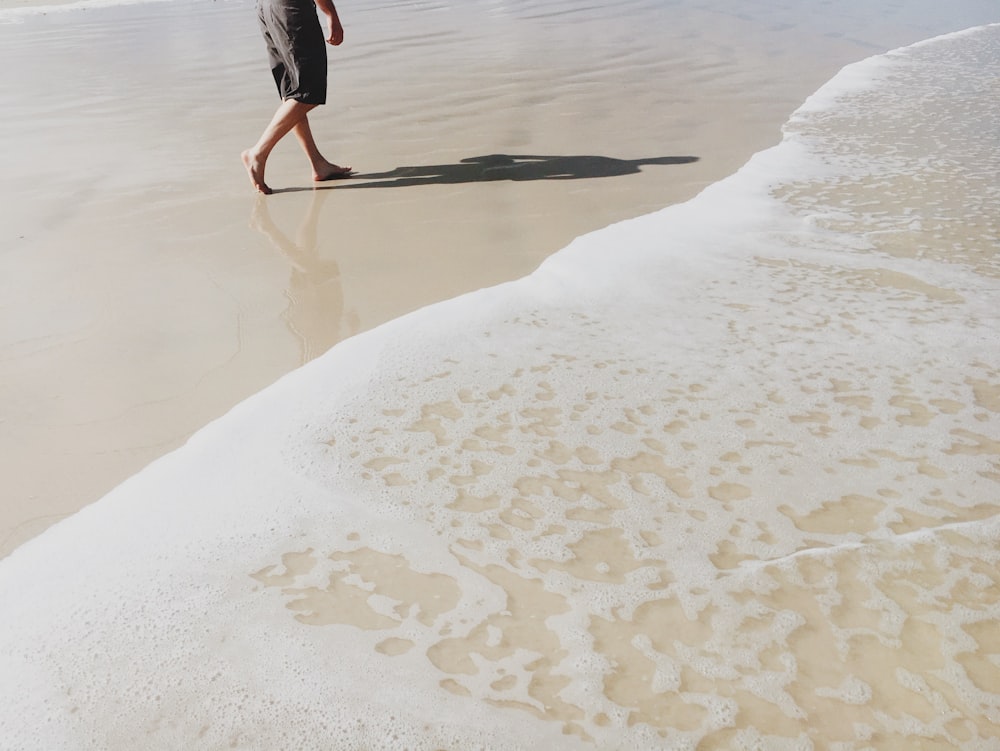 회색 반바지를 입은 남자가 해변을 걷고 있습니다.