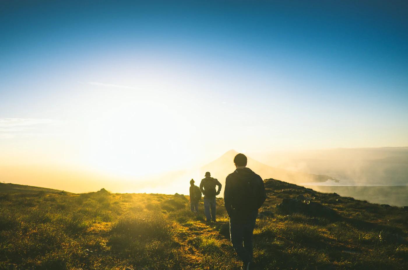 Silhouette of three men walking together in a line across a sunlit ridge at golden hour