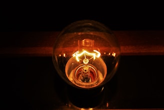 A glowing incandescent light bulb with a visible filament emits a warm, yellow-orange light against a dark background.