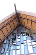 A close-up of a building's roof structure, featuring a steep gable design with wooden beams and textured glass panels. The architecture highlights a mixture of traditional and modern elements, with prominent use of natural materials.