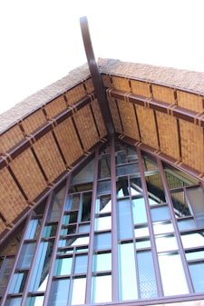 A close-up of a building's roof structure, featuring a steep gable design with wooden beams and textured glass panels. The architecture highlights a mixture of traditional and modern elements, with prominent use of natural materials.