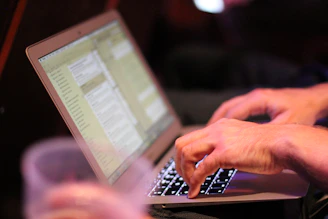 Close-up of hands typing quickly on a keyboard with documents beside the laptop.