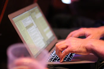 Close-up of hands typing on a laptop with paperwork nearby.
