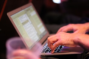 Close-up of hands working on a laptop with business documents nearby.