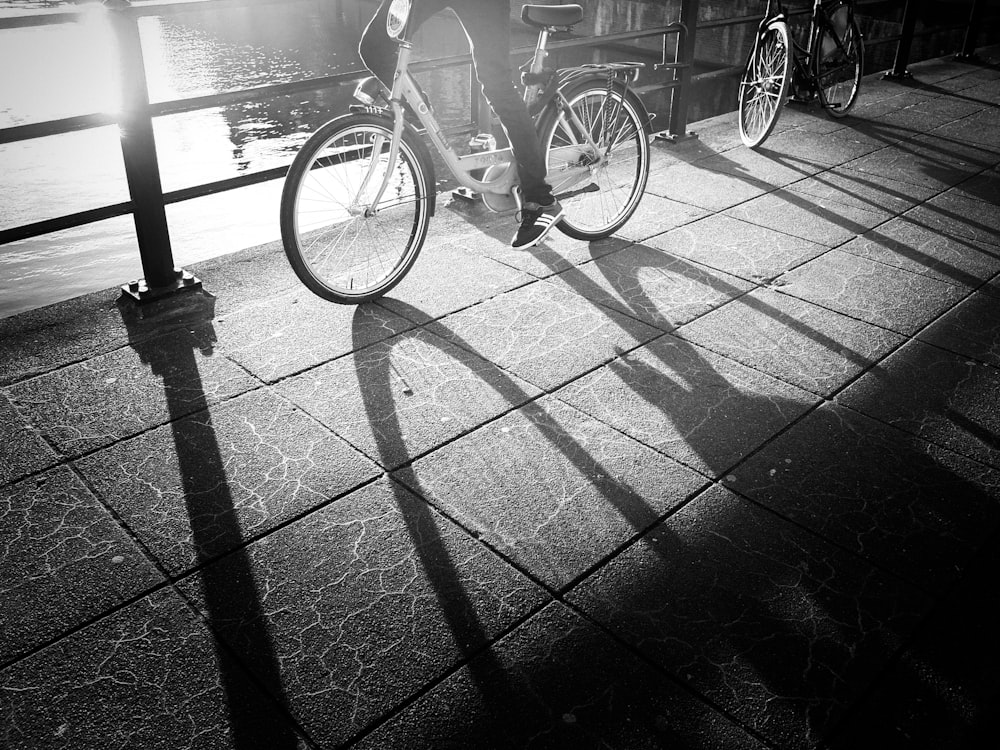 grayscale photo of a person wearing sneakers riding a bicycle