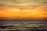 A serene ocean view at sunset with orange and yellow hues filling the sky. Gentle waves ripple across the surface of the water, creating a calm and peaceful atmosphere.