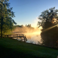 A serene lake at sunrise with a small wooden dock and mist rising from the water.