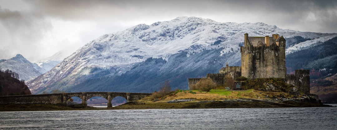 gray concrete bridge near mountain at daytime, Eilean Donan Castle on a cloudy day