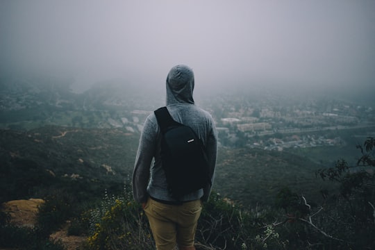 man in gray hoodie with black backpack looking at the city from mountain peek in Cowles Mountain United States