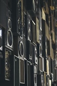 Multiple speaker boxes are arranged in a grid-like pattern, creating a textured and layered visual effect. The speakers vary in size and design, with some displaying intricate details and others having a minimalist appearance.