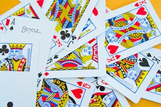 A collection of playing cards scattered on a flat surface includes a variety of face cards such as kings and jacks, as well as aces. The cards display intricate designs in vibrant colors, including red, blue, yellow, and black suits.