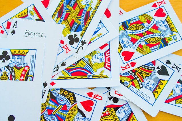 A collection of playing cards scattered on a flat surface includes a variety of face cards such as kings and jacks, as well as aces. The cards display intricate designs in vibrant colors, including red, blue, yellow, and black suits.