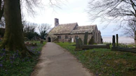 The churchyard at Bramham Sanctum with weathered gravestones and blooming wildflowers.
