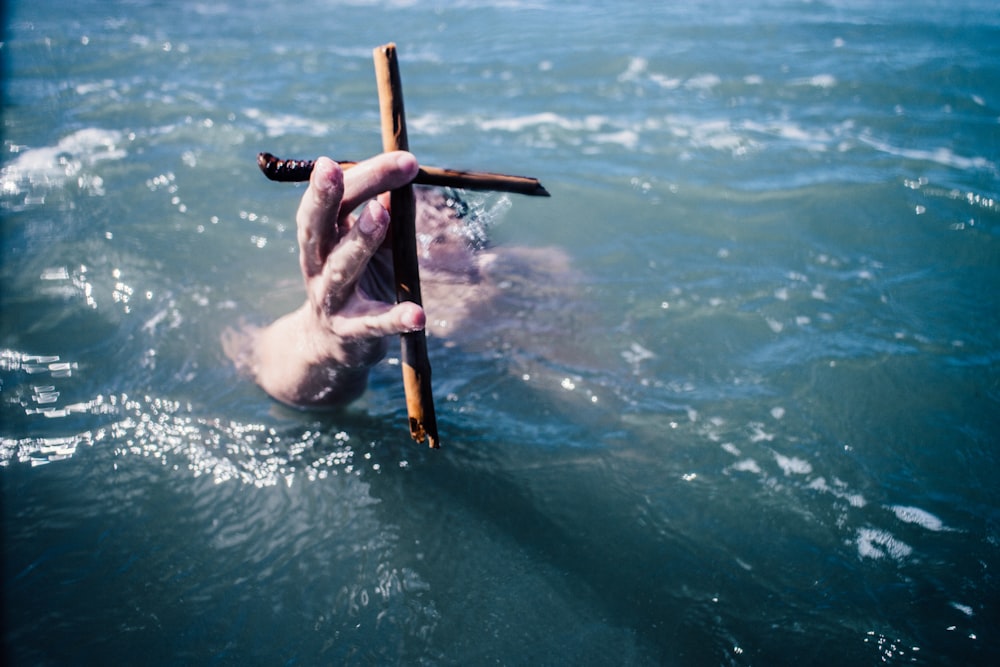 person under water holding brown wooden cross above water at daytime