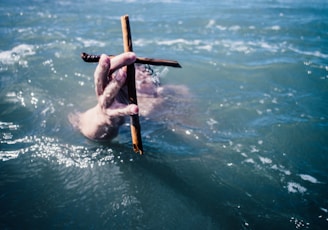 person under water holding brown wooden cross above water at daytime