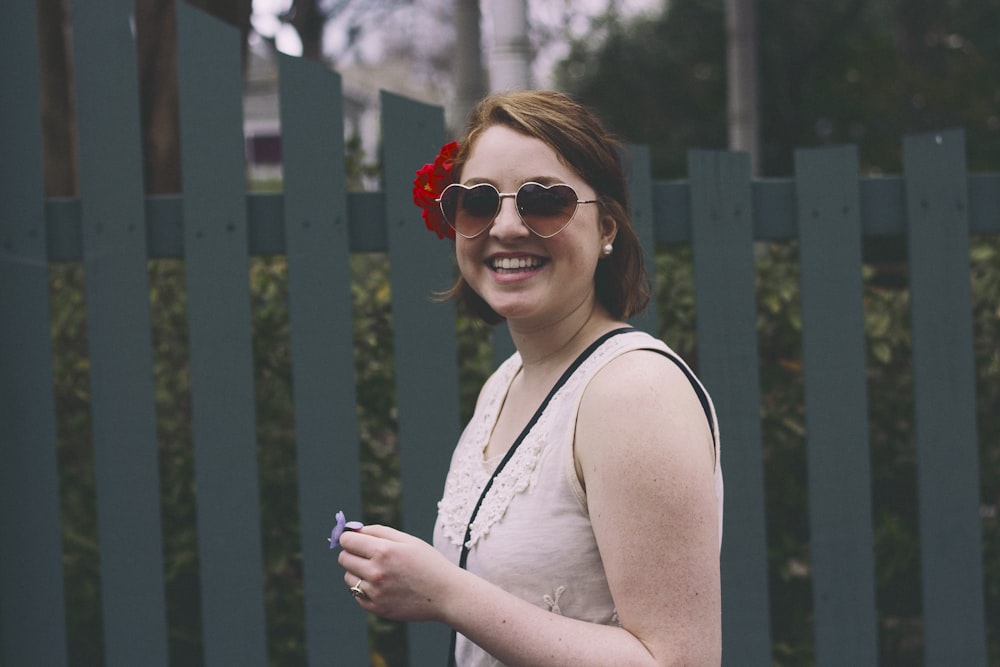 mulher em pé enquanto sorri ao lado da cerca de madeira azul