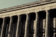 A grand neoclassical building with large stone columns supports a façade inscribed with the words 'FACULTAD DE DERECHO Y CIENCIAS.' The architectural style reflects an imposing and formal design, characteristic of institutional or governmental structures.