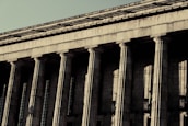 A grand neoclassical building with large stone columns supports a façade inscribed with the words 'FACULTAD DE DERECHO Y CIENCIAS.' The architectural style reflects an imposing and formal design, characteristic of institutional or governmental structures.