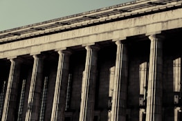 A grand neoclassical building with large stone columns supports a façade inscribed with the words 'FACULTAD DE DERECHO Y CIENCIAS.' The architectural style reflects an imposing and formal design, characteristic of institutional or governmental structures.