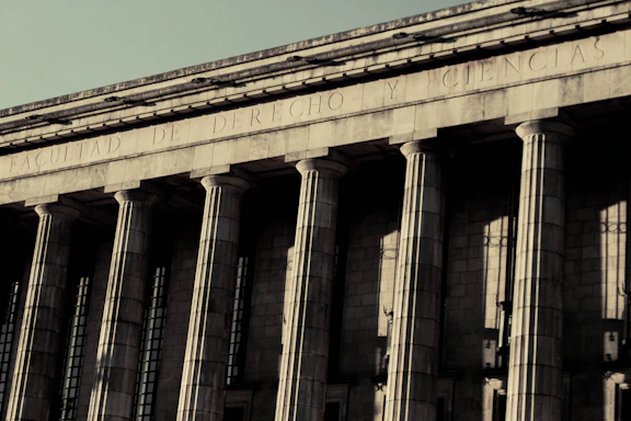 A grand neoclassical building with large stone columns supports a façade inscribed with the words 'FACULTAD DE DERECHO Y CIENCIAS.' The architectural style reflects an imposing and formal design, characteristic of institutional or governmental structures.