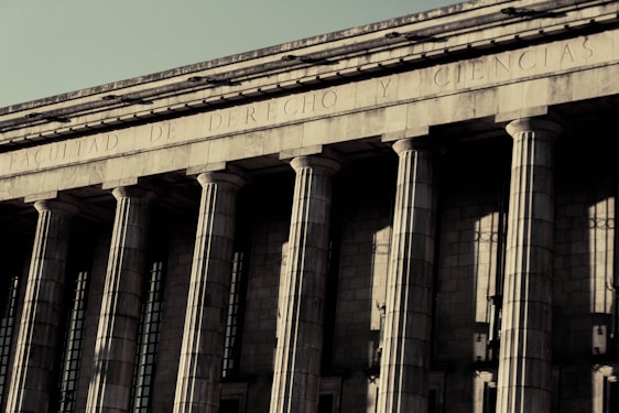 A grand neoclassical building with large stone columns supports a façade inscribed with the words 'FACULTAD DE DERECHO Y CIENCIAS.' The architectural style reflects an imposing and formal design, characteristic of institutional or governmental structures.