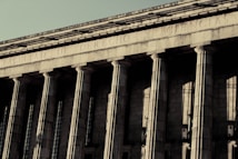 A grand neoclassical building with large stone columns supports a fa&ccedil;ade inscribed with the words 'FACULTAD DE DERECHO Y CIENCIAS.' The architectural style reflects an imposing and formal design, characteristic of institutional or governmental structures.
