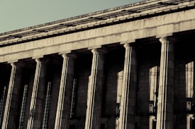 A grand neoclassical building with large stone columns supports a fa&ccedil;ade inscribed with the words 'FACULTAD DE DERECHO Y CIENCIAS.' The architectural style reflects an imposing and formal design, characteristic of institutional or governmental structures.