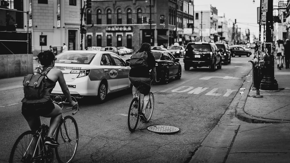 grayscale photo of two person riding bicycle on road