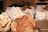 Various artisan breads placed on a burlap-covered table, with two distinct loaves prominently displayed in the foreground. Each loaf has a unique pattern or scoring on the crust and is surrounded by paper bags labeled with different types of bread, such as 'Red Fife Glenn Boule' and 'Sonora Country Blonde'.