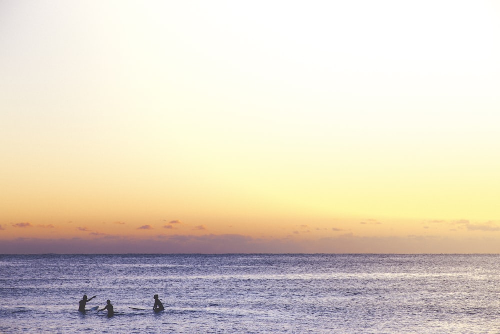 three person playing on ocean during golden hour