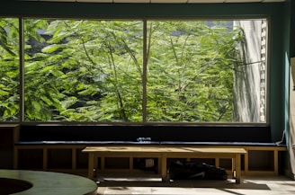 A serene hostel lounge bathed in warm beige and muted sage, with natural light filtering through large windows.