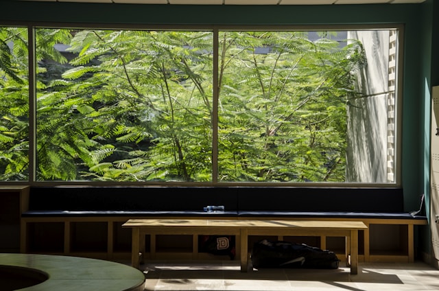 A serene hostel lounge bathed in warm beige and muted sage, with natural light filtering through large windows.