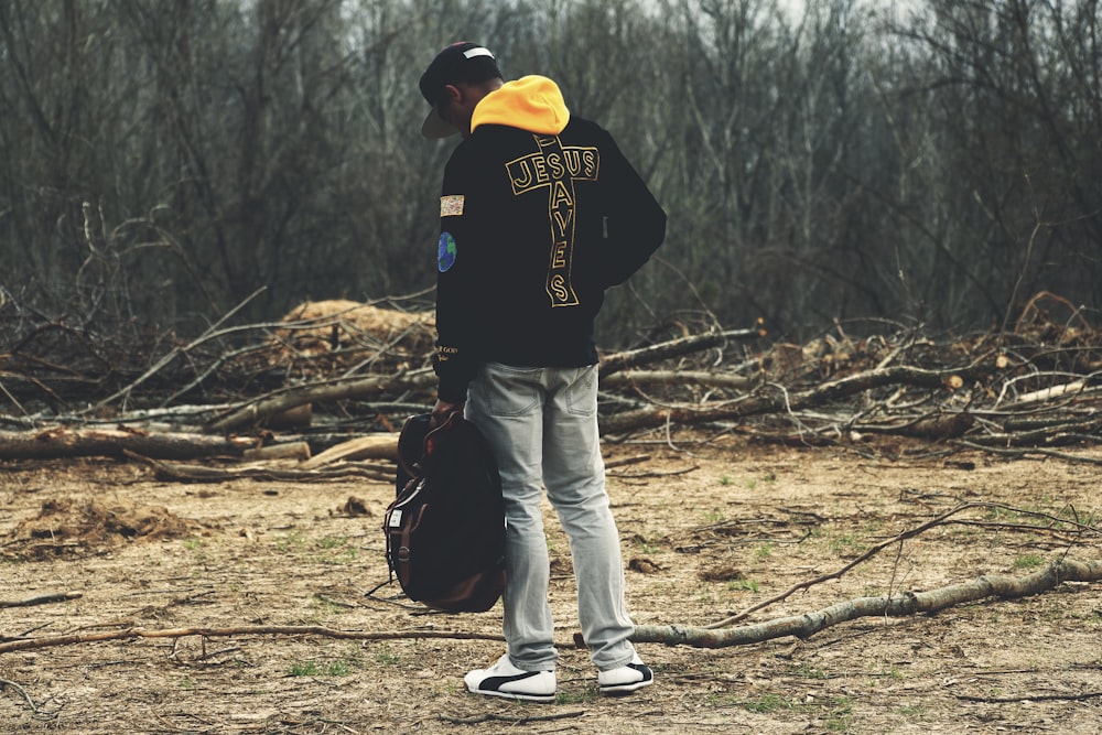 man in gray denim pants and black hoodie holding bag looking down