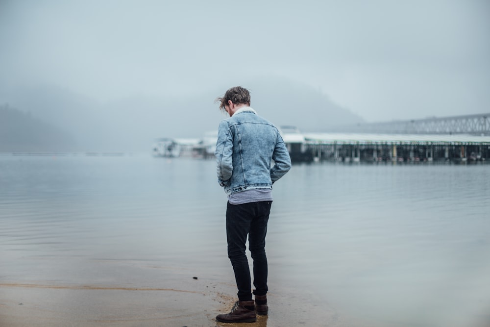 Mann in blauer Jeansjacke steht am Ufer