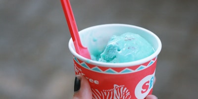 Close-up of a hand holding a Big Love mini cup with a bright pink spoon against a green and white backdrop.