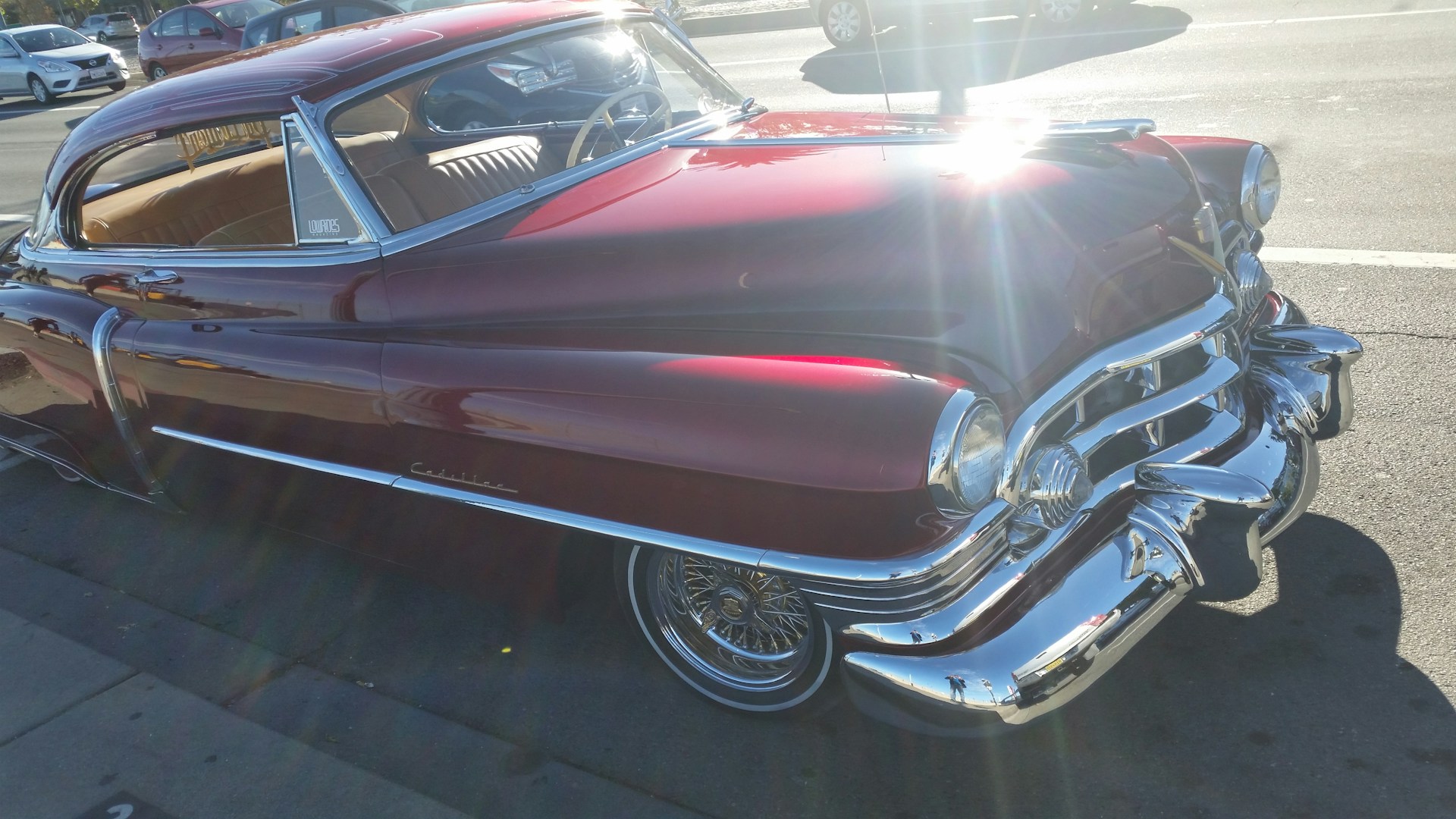 A classic car parked on a quiet street, its glossy red paint reflecting the soft afternoon light.