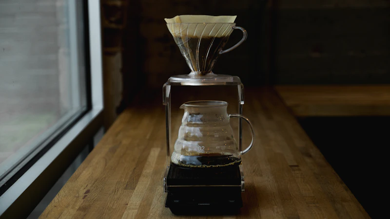 A glass V60 and its paper filter on a carafe, by a window