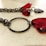 A close-up view of a piece of jewelry with dark metal chains and vibrant red gems. The gems have a polished, faceted surface, giving them a bright and lustrous appearance. The metal chain features a circular link and heart-shaped detail.