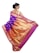 A woman is elegantly draped in a traditional saree with vibrant colors and intricate patterns. The saree features a rich combination of purple and gold with decorative motifs, including peacocks and floral designs. Her hair is styled in an elegant updo, and she accessorizes with earrings.