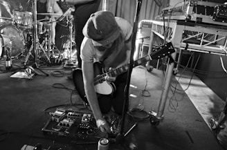 Guitarist adjusting a vintage-style overdrive pedal under warm stage lights.