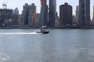 A sleek motorboat docked beside a pier with a city skyline in the background.