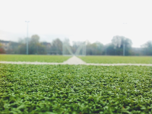 Close-up of a football rolling on the green turf with the academy’s goalpost in the background.