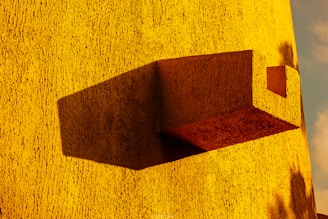 Abstract architectural sculpture with layered shadows and warm yellow accents on a dark background.