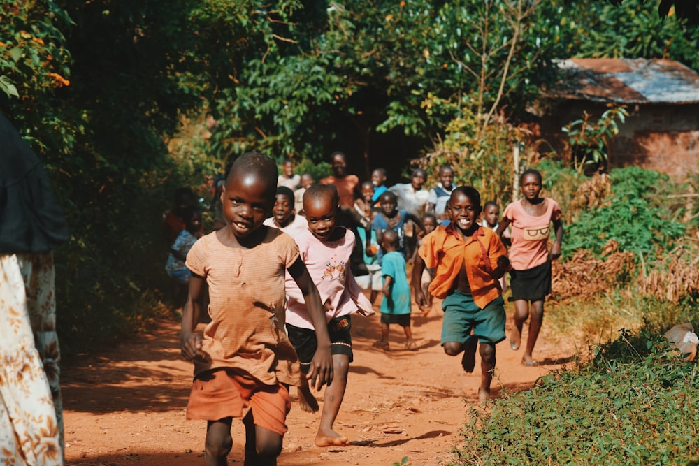 niños corriendo y caminando sobre arena marrón rodeada de árboles durante el día